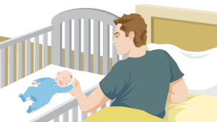 A father is lying in bed and holding hands with his baby, who is lying in a crib beside the bed